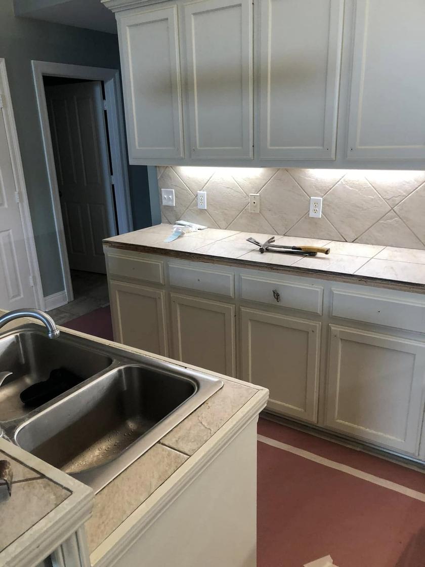 Before: a kitchen with cream cabinets, the hardware off and the old tile counter being torn out