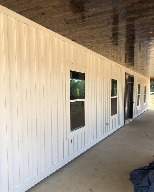 A white board-and-batten porch wall with a stained plank ceiling