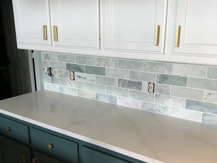 Teal lower cabinets with brass pulls under a stone subway-tile backsplash