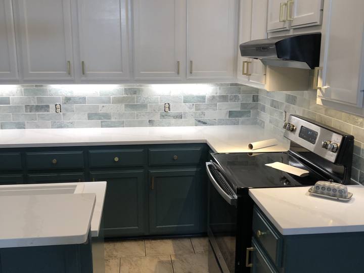 A kitchen with white upper cabinets, teal lower cabinets and brass pulls