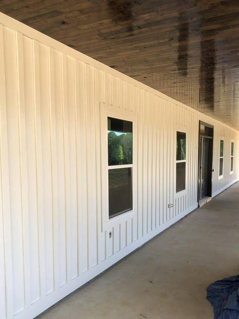 A board-and-batten porch wall with a stained plank ceiling and a black door