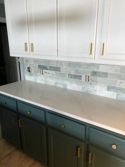 Teal lower cabinets with brass pulls under a stone subway backsplash