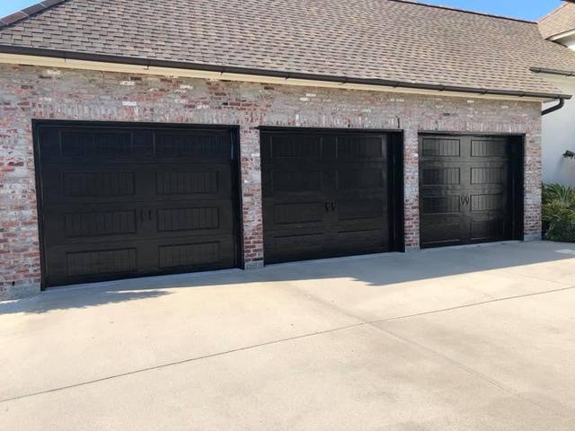 Three raised-panel garage doors painted black on whitewashed brick