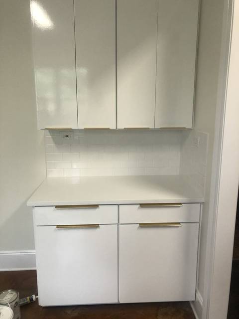 A run of high-gloss white cabinets with brass pulls